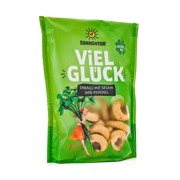 SONNENTOR Good Luck Taralli with sesame and fennel, green packaging with illustration of a young woman with a large lucky clover and viewing window. The ring-shaped, gluten-free snack can be seen through the viewing window.