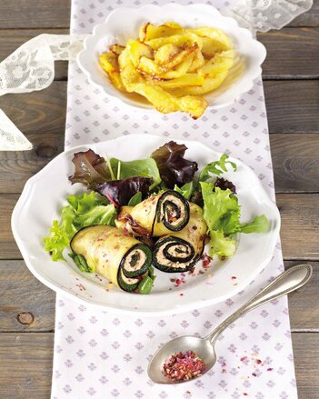 Auf dem Foto sind Melanzani-Röllchen mit Blattsalat auf einem weißen Teller zu sehen. Dahinter steht ein weiterer Teller mit Kartoffelchips. | © SONNENTOR