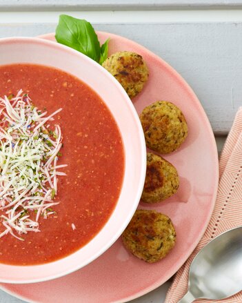 Auf dem Foto sieht man eine Tomaten-Basilikum-Suppe mit Parmesan. Auf dem Unterteller sieht man Hirse-Parmesanbällchen. | © SONNENTOR