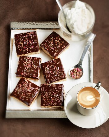 Auf dem Foto sind mehrere Stück Schokokuchen auf einem silbernen Tablett zu sehen. Der Kuchen ist mit Blüten dekoriert. | © SONNENTOR