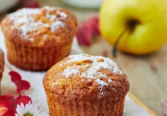 Auf dem Foto sieht man zwei Muffins. Daneben liegt ein Gänseblümchen und dahinter ist ein Apfel zu sehen. | © SONNENTOR