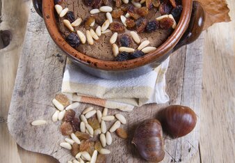 Auf dem Foto ist eine Auflaufform mit Castagnoccio, Toskanischen Kastanienmehlkuchen zu sehen. Davor liegen Kastanien. | © SONNENTOR