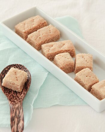 Auf einem weißen Servicetablett sind die hellen Chai Shortbread zu sehen. Daneben liegt ein Holzlöffel mit einem Chai Shortbread darauf. | © SONNENTOR