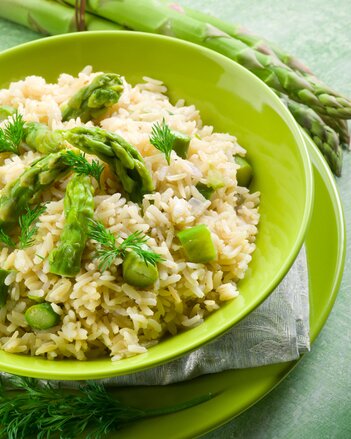 Auf dem Foto sieht man eine Schüssel mit Spargelrisotto. Dahinter ist ebenso grüner Spargel zu sehen. | © SONNENTOR