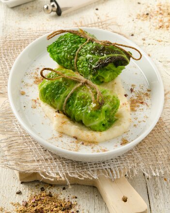 Auf dem Foto sind zwei Stück Emmer-Kohl-Rouladen auf Pastinaken-Apfel Creme zu sehen. Rundherum sind Gewürze verteilt. | © SONNENTOR