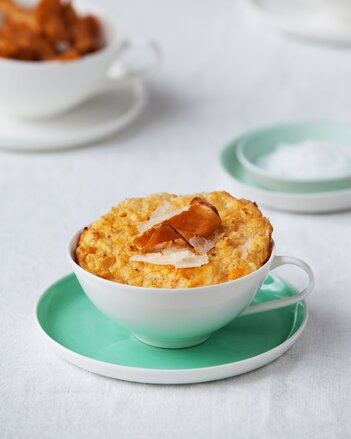 Auf dem Foto sieht man eine Tasse mit einem Süßkartoffelküchlein darin. Das Küchlein ist mit Parmesan und Süßkartoffelchips garniert. | © SONNENTOR