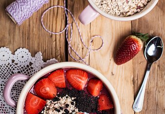 Foto einer Beeren Smoothie Bowl mit Superfood Topping. Daneben sieht man einen Löffel, eine Erdbeere und Haferflocken. | © SONNENTOR