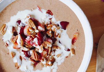 Auf dem Foto sieht man eine Schale Rosenblüten-Frappé Porridge mit Nüssen darauf. Rund um die Schüssel sind Rosenblüten verteilt. | © SONNENTOR