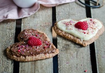 Auf dem Foto sind zwei Herzen zu sehen. Einmal mit heller und einmal mit dunkler Schokolade. Darauf sind Gewürzblüten und Himbeeren zu sehen. | © SONNENTOR