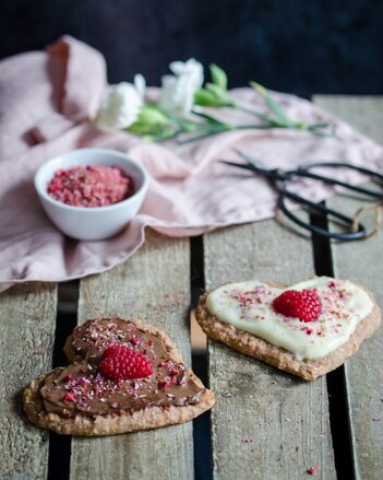 Auf dem Foto sind zwei Herzen zu sehen. Einmal mit heller und einmal mit dunkler Schokolade. Darauf sind Gewürzblüten und Himbeeren zu sehen. | © SONNENTOR