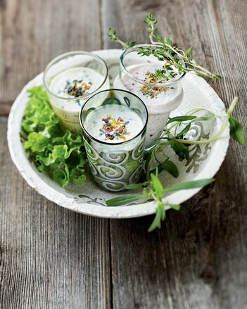 Auf dem Foto sind drei Gläser mit dem Gewürz-Joghurtdressing zu sehen. Rundherum sind frische Kräuter und frischer Salat zu sehen. | © SONNENTOR