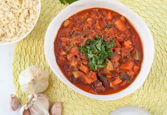 Auf dem Foto ist ein Teller mit Kichererbsen-Gemüse-Tajine zu sehen. Daneben sieht man Knoblauch, Gewürze, Zitronen und Petersilie. | © SONNENTOR