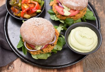 Auf dem Foto ist eine Pfanne mit zwei Holy Veggie Burgern zu sehe. Darauf sieht man auch eine Schale mit Dip und eine Schale mit buntem Gemüse. | © SONNENTOR