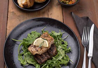 Auf dem Foto sieht man zwei Steaks auf Rucola Salat. Dahinter sind Baguettes zu sehen. | © SONNENTOR