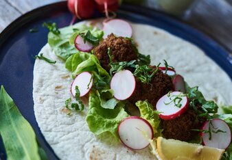 Auf dem Foto sieht man einen Wrap mit Wildkräuterfalafel, Salat und Radieschen zu sehen. Dahinter sieht man ein Gläschen mit Dip. | © SONNENTOR