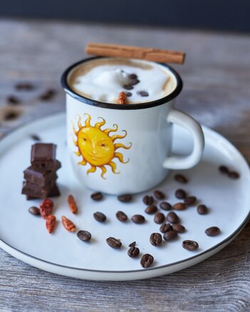 Auf dem Foto ist eine SONNENTOR Tasse mit Mexican Coffee zu sehen. Daneben liegen Kaffeebohnen, Chilischoten und Schokolade. | © SONNENTOR