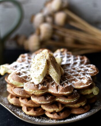 Auf dem Foto sieht man einen Teller mit mehreren Topfen-Mohn Waffeln übereinander zu sehen. Sie sind mit Bananenscheiben und Flower Power Gewürz garniert. | © SONNENTOR