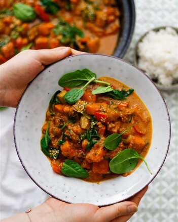 Auf dem Foto sieht man einen Teller mit Süßkartoffelcurry mit Spinat. Man sieht wie jemand den Teller hält. | © SONNENTOR