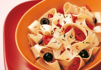 Auf dem Foto ist ein orangenes Schälchen mit Scharfmacher-Pasta zu sehen. In der Pasta sind auch Oliven und Tomaten zu sehen. | © SONNENTOR