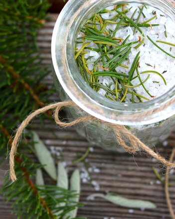 Auf dem Foto ist ein Schälchen mit dem Waldbadesalz zu sehen. Darauf sind Fichtennadeln verteilt. Um das Glas herum sind auch Fichtenzweige verteilt. | © Valerie Jarolim