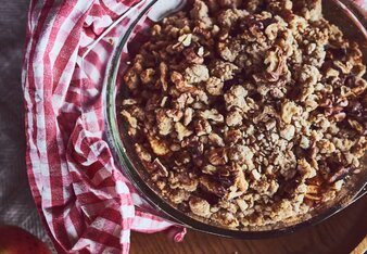 Auf dem Foto ist eine Form mit Apfel-Cranberry-Crumble zu sehen. Daneben liegen Zimtstangen und ein Apfel. | © SONNENTOR