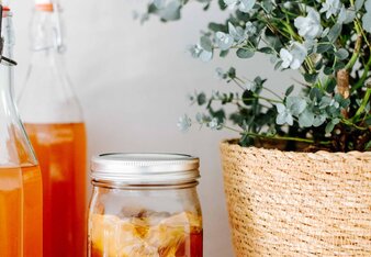 Auf dem Foto sieht man drei Flaschen mit Kombucha. Daneben sieht man ein Glas mit Kombucha mit Eis. | © SONNENTOR