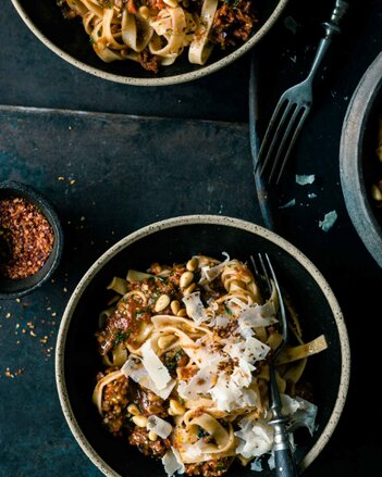 Auf dem Foto ist ein schwarzer Teller mit Tomatenpesto Pasta zu sehen. Darüber sind Nüsse, Parmesan und Chiliflocken gestreut. | © SONNENTOR