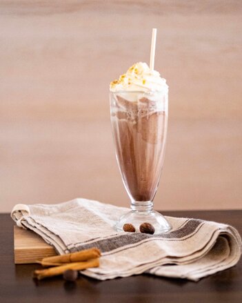 Auf dem Foto ist ein Eisbecher mit Schlaukakao zu sehen. Davor sieht man Zimtstangen. | © SONNENTOR