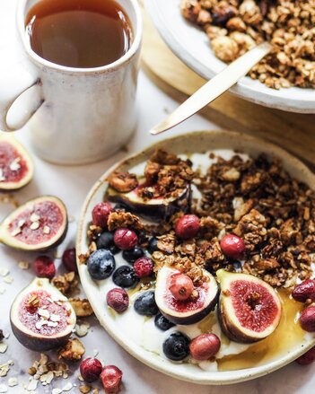 Auf dem Foto ist ein Teller mit Granola und frischen Früchten zu sehen. Daneben steht eine Tasse Rooibos Orangen Tee. | © SONNENTOR