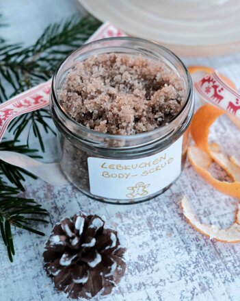 Auf dem Foto ist ein Glas Lebkuchen Body Scrup zu sehen. Daneben liegen Mandarinenschalen, Zapfen und ein Zweig. | © SONNENTOR