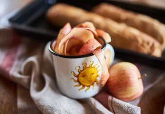 Auf dem Foto sieht man eine Sonnentor Tasse mit Apfelschale. Im Hintergrund sieht man auf einem Blech zwei Strudel. | © SONNENTOR