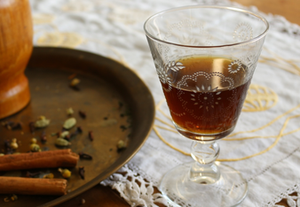 Auf dem Foto sieht man ein Glas mit Kräuterbitter. Daneben sieht man Kardamom, Nelken und Zimt. | © SONNENTOR