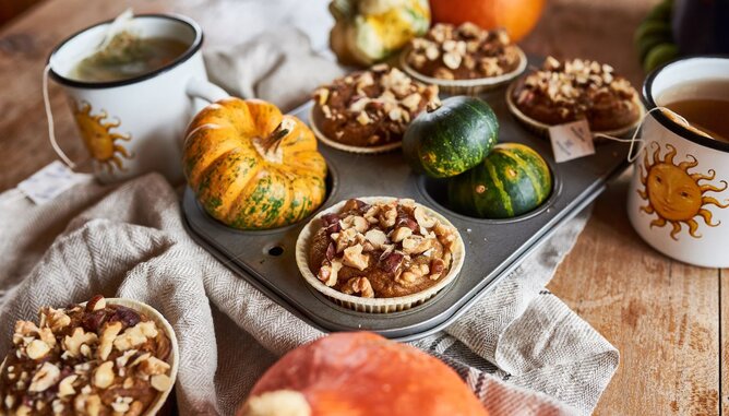 Auf dem Foto sind Kürbismuffins zu sehen. Sie sind mit Nüssen garniert. Daneben sieht man kleine Kürbisse und zwei Tassen Tee. | © SONNENTOR