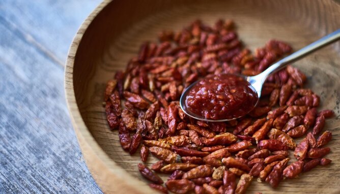 Auf dem Foto sieht man eine Holzschale mit Chilischoten darin. Darauf liegt ein Löffel mi Harissa Paste. | © SONNENTOR